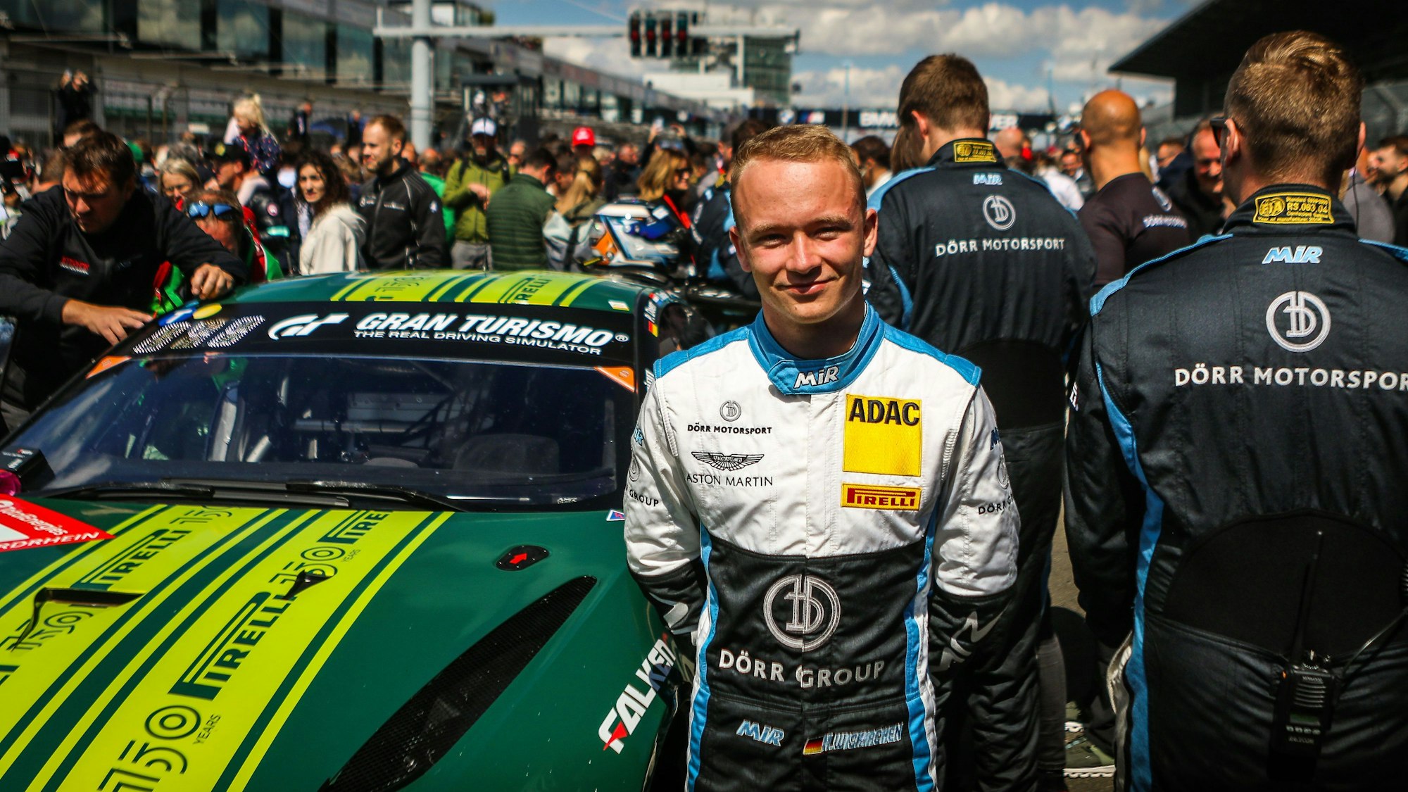 Moritz Wiskirchen steht beim 24-Stunden-Rennen 2022 vor einem Aston Martin. In der Boxengasse im Hintergrund sind viele Menschen.