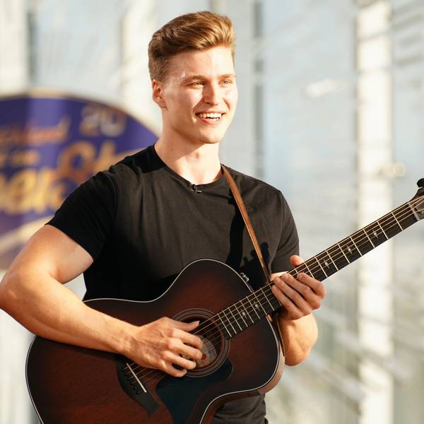 Nico Grund steht mit seiner Gitarre vor dem Logo von Deutschland sucht den Superstar.
