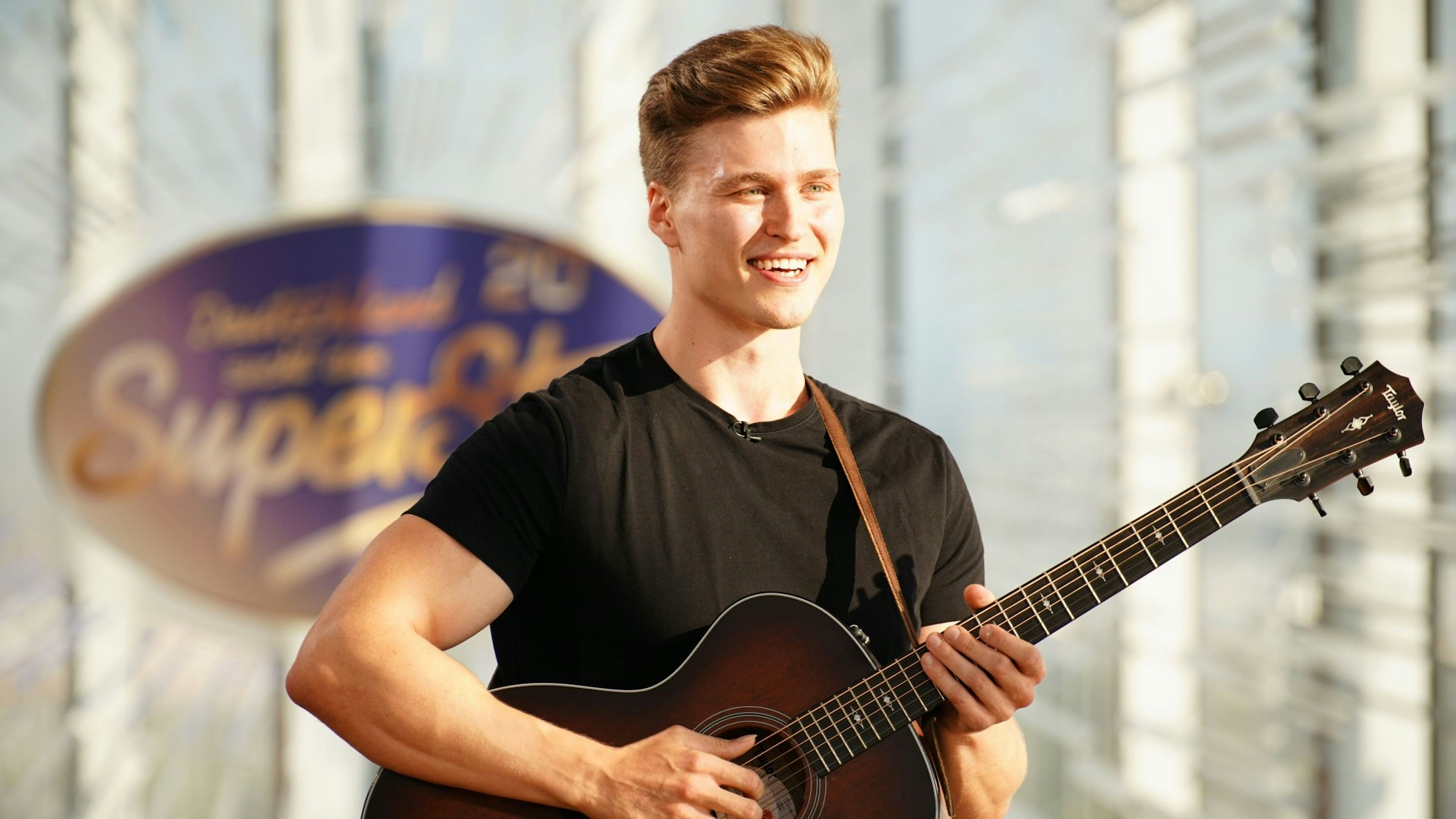 Nico Grund steht mit seiner Gitarre vor dem Logo von Deutschland sucht den Superstar.