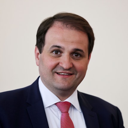 Nathanael Liminski (CDU), Chef der Staatskanzlei des Landes Nordrhein-Westfalen, steht vor einer weißen Wand. Er trägt einen blauen Anzug.