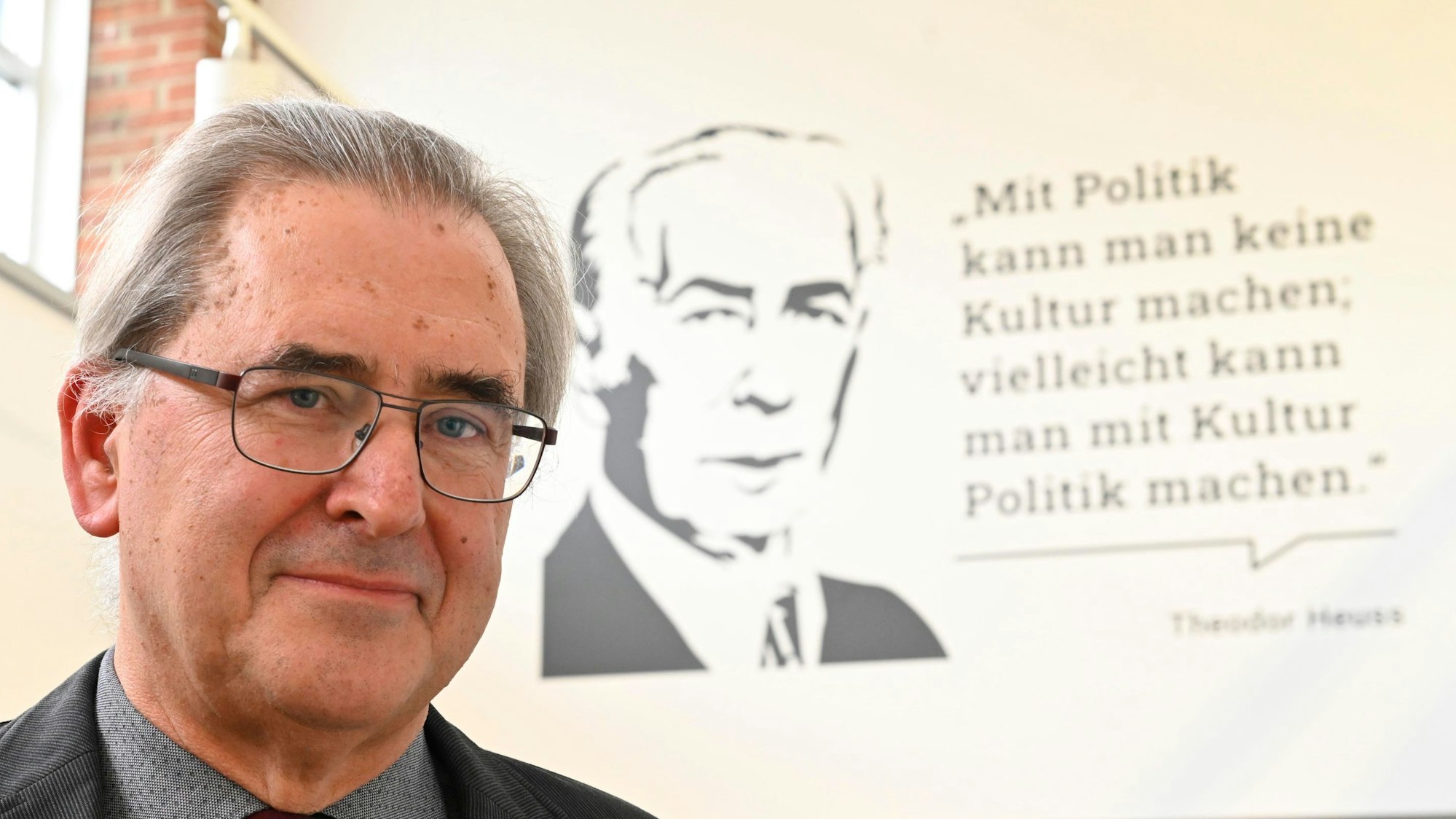 Klaus Füßmann steht vor einem Zitat von Theodor Heuss an einer Wand. Das Zitat lautet: „Mit Politik kann man keine Kultur machen, vielleicht kann man mit Kultur Politik machen.“