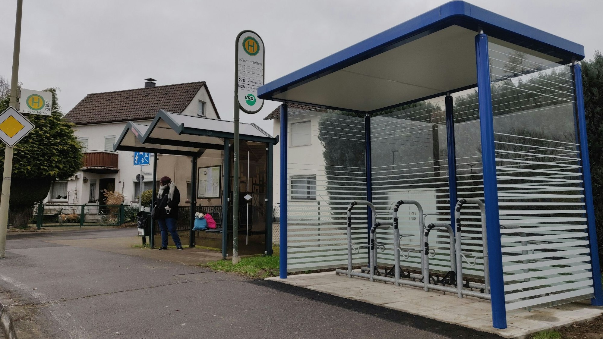 An der Bushaltestelle in Büscherhöfen steht neben dem Wartehäuschen für Busfahrgäste ein neuer blauer verglaster Unterstand mit Schlossbügeln für Radfahrer.
