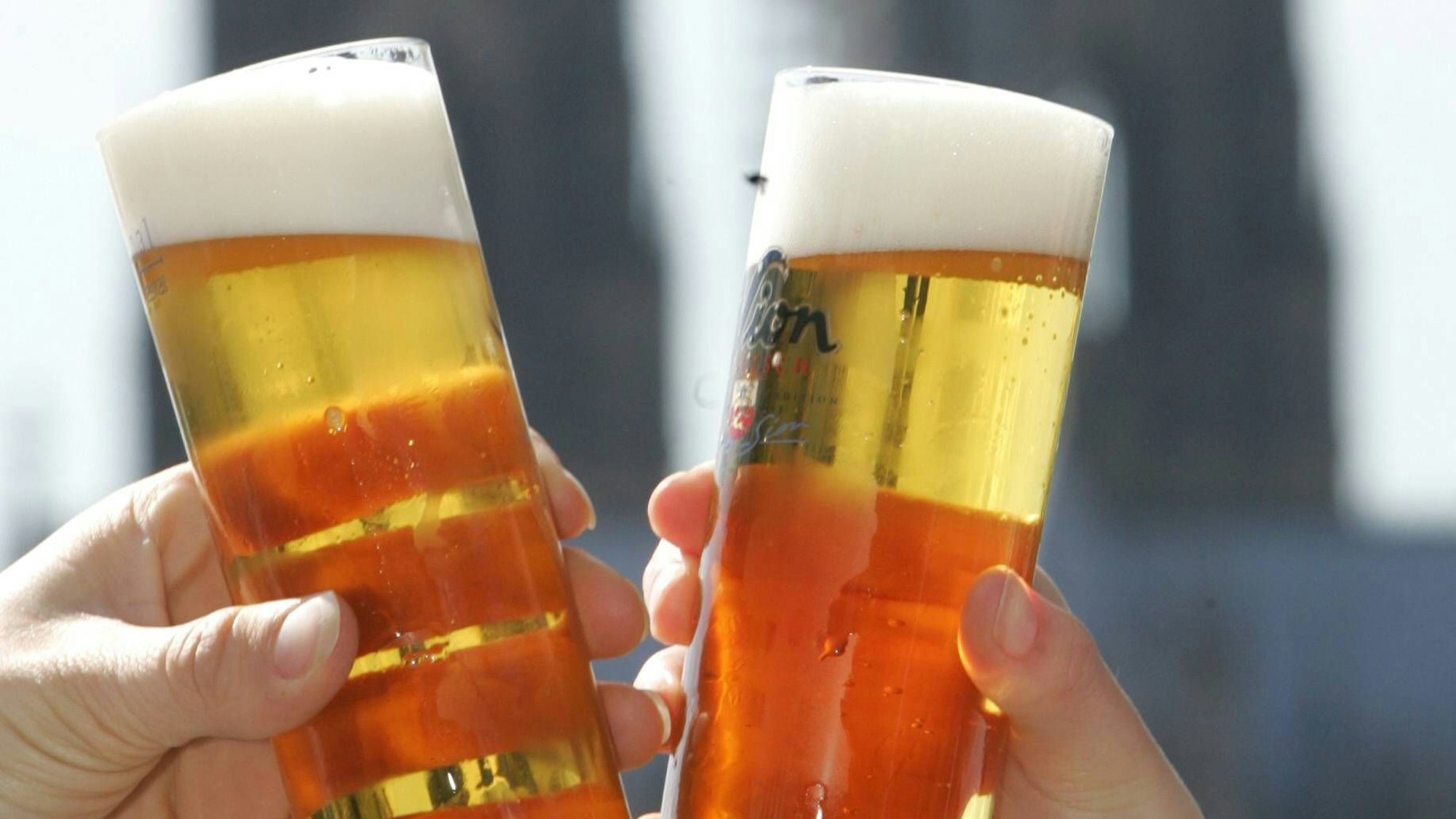 Zwei Menschen stoßen vor dem Dom mit Kölsch an.