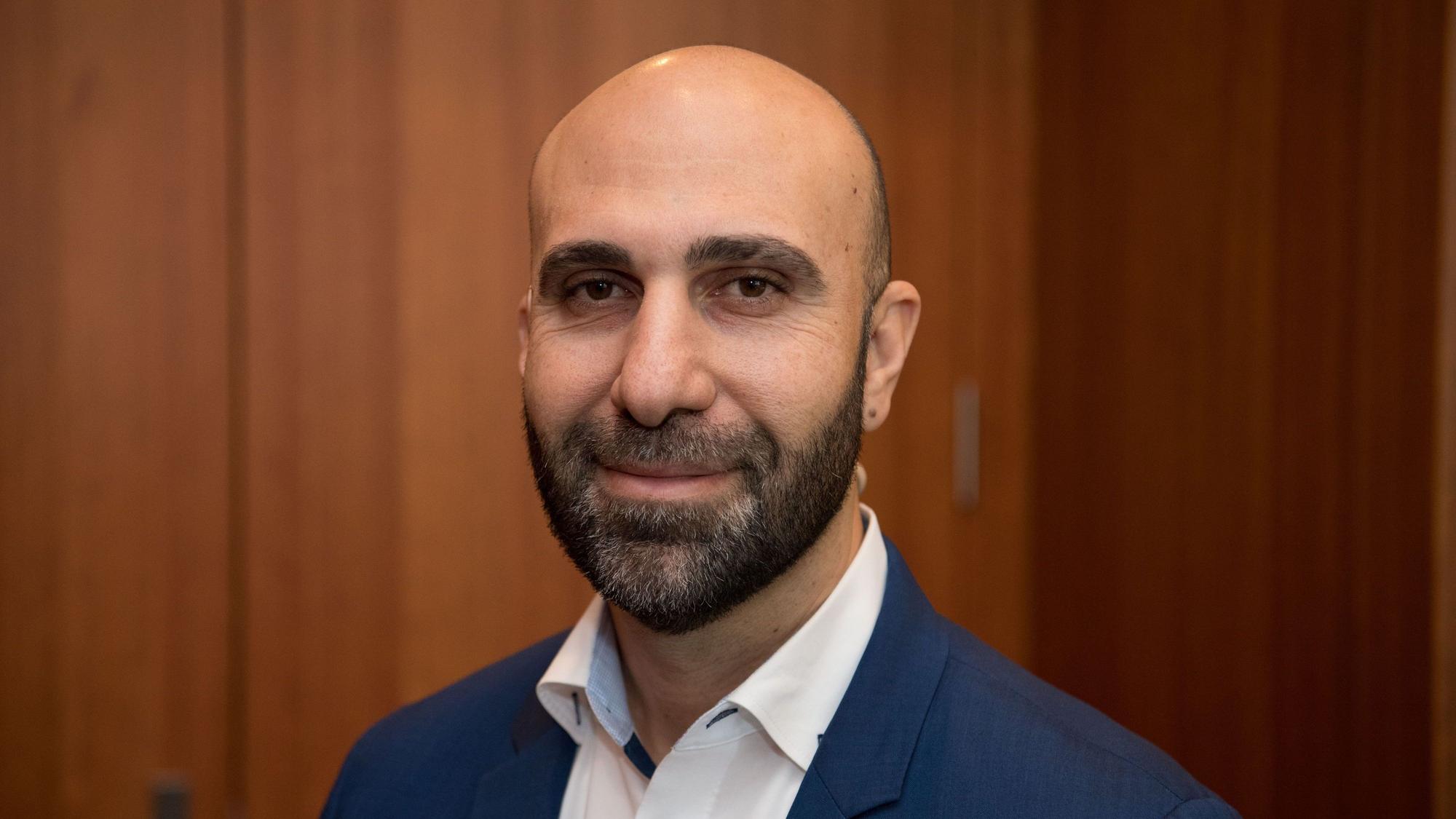 Der Psychologe Ahmad Mansour steht vor einer Holztür.