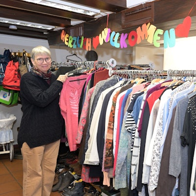 Christa Küppers steht an einer Kleiderstange, vollbehangen mit Kleidung.
