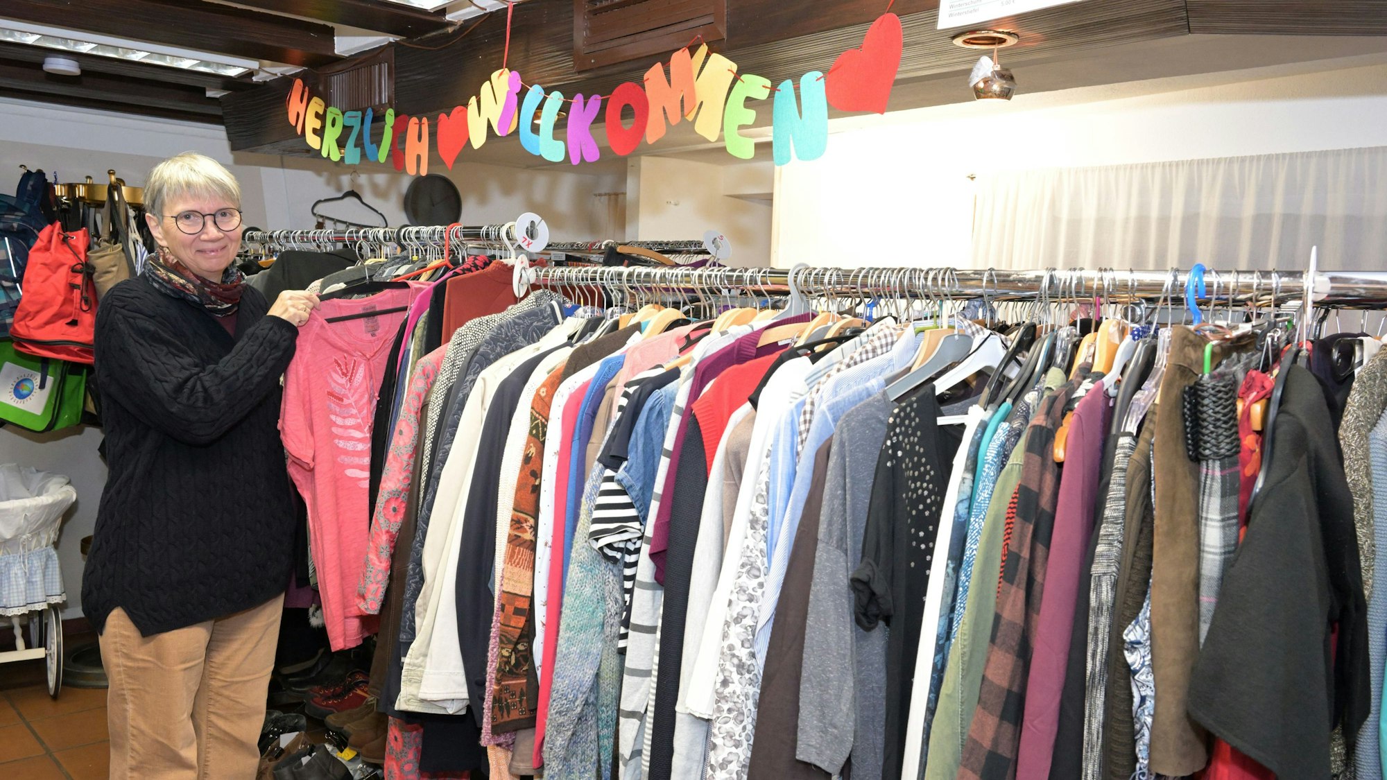 Christa Küppers steht an einer Kleiderstange, vollbehangen mit Kleidung.