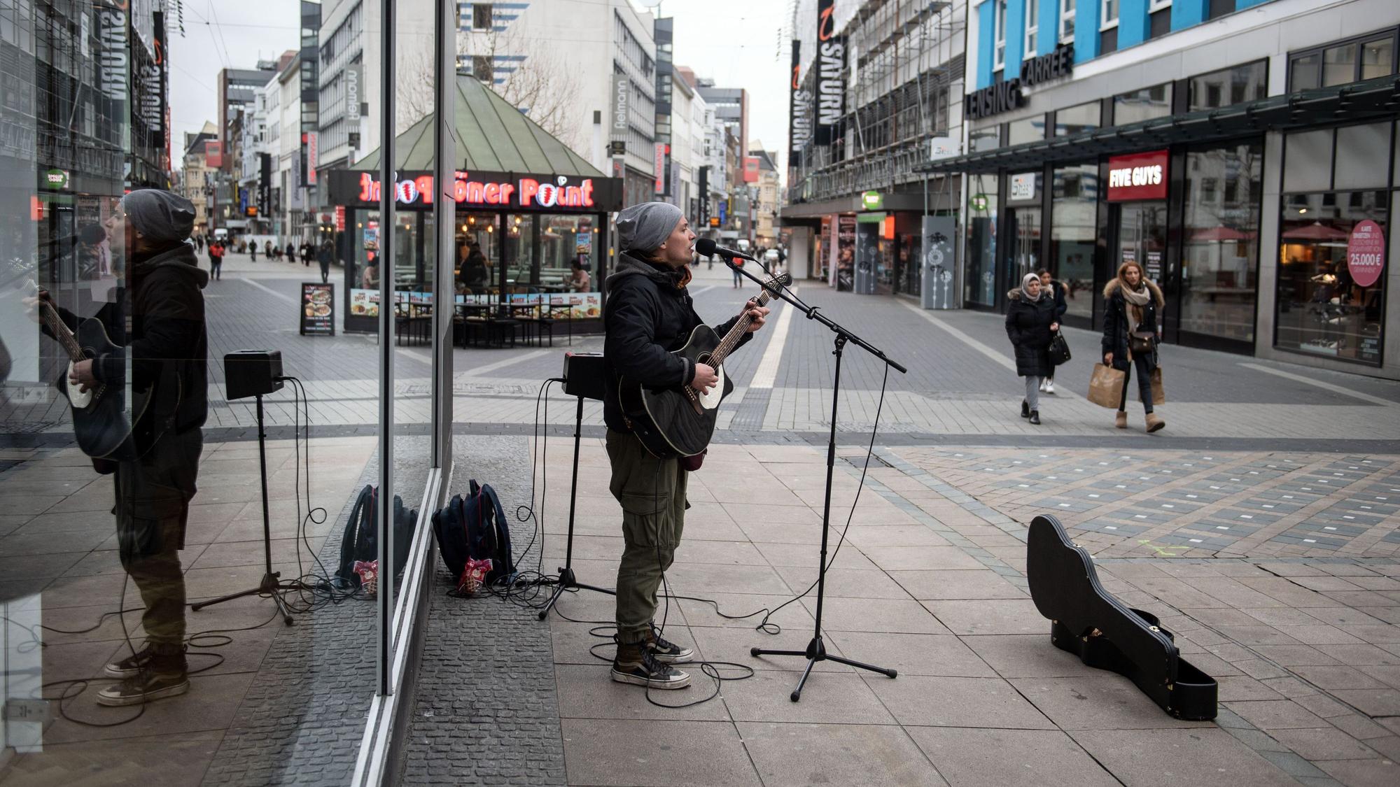 Ein Straßenmusiker spielt in der Fußgängerzone auf seiner Gitarre und singt.