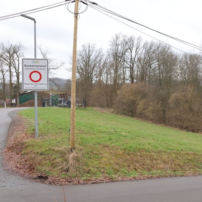 Auf einem Stück Wiese steht ein weißes Schild, auf dem ein roter Kreis zu sehen ist. Darüber steht das Wort Baubetriebshof.