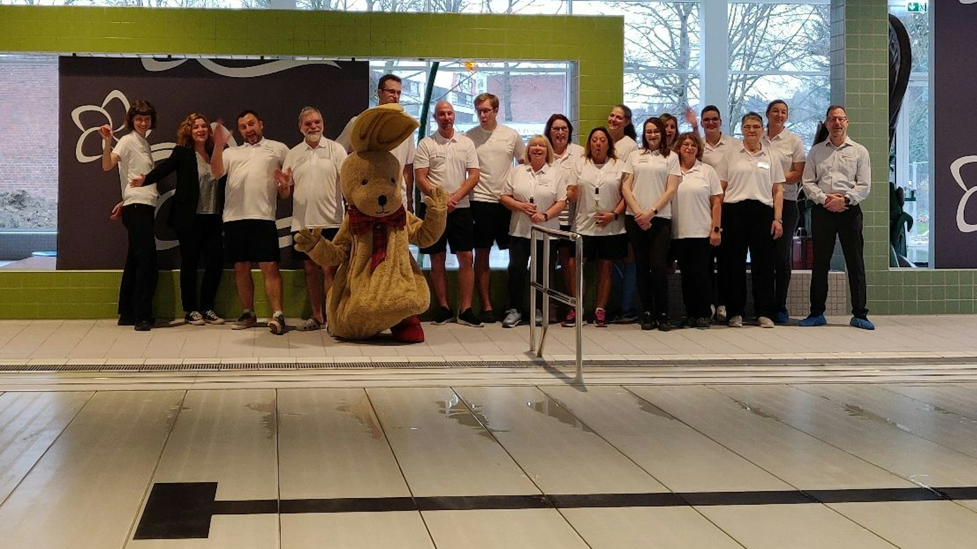 Das Team des Blütenbads steht in weißen Bad-T-Shirts mit Maskottchen Hase Felix am Schwimmbecken.