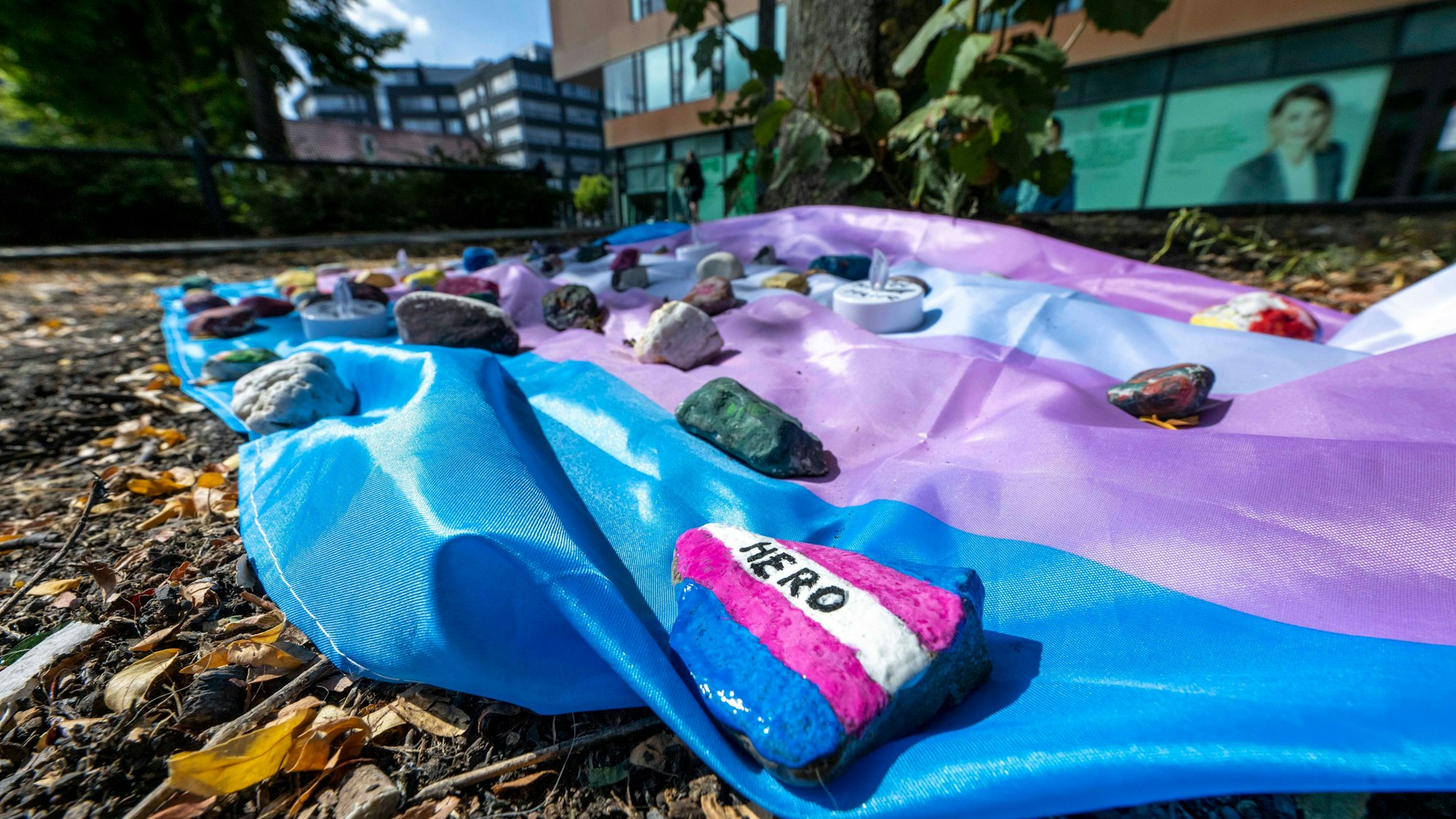 Menschen haben auf dem Hafenplatz eine Fahne ausgelegt, die mit bemalten Steinen beschwert ist. Auf einem steht "Hero" zu lesen.