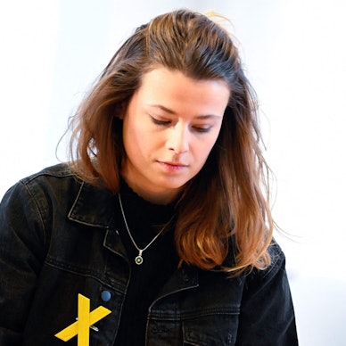 Die deutsche Klimaschutzaktivistin Luisa Neubauer vor einem Fenster. Auf ihrer schwarzen Jacke trägt sie ein gelbes X, um sich mit dem Widerstand gegen den Abriss des Braunkohledorfs Lützerath zu solidarisieren.