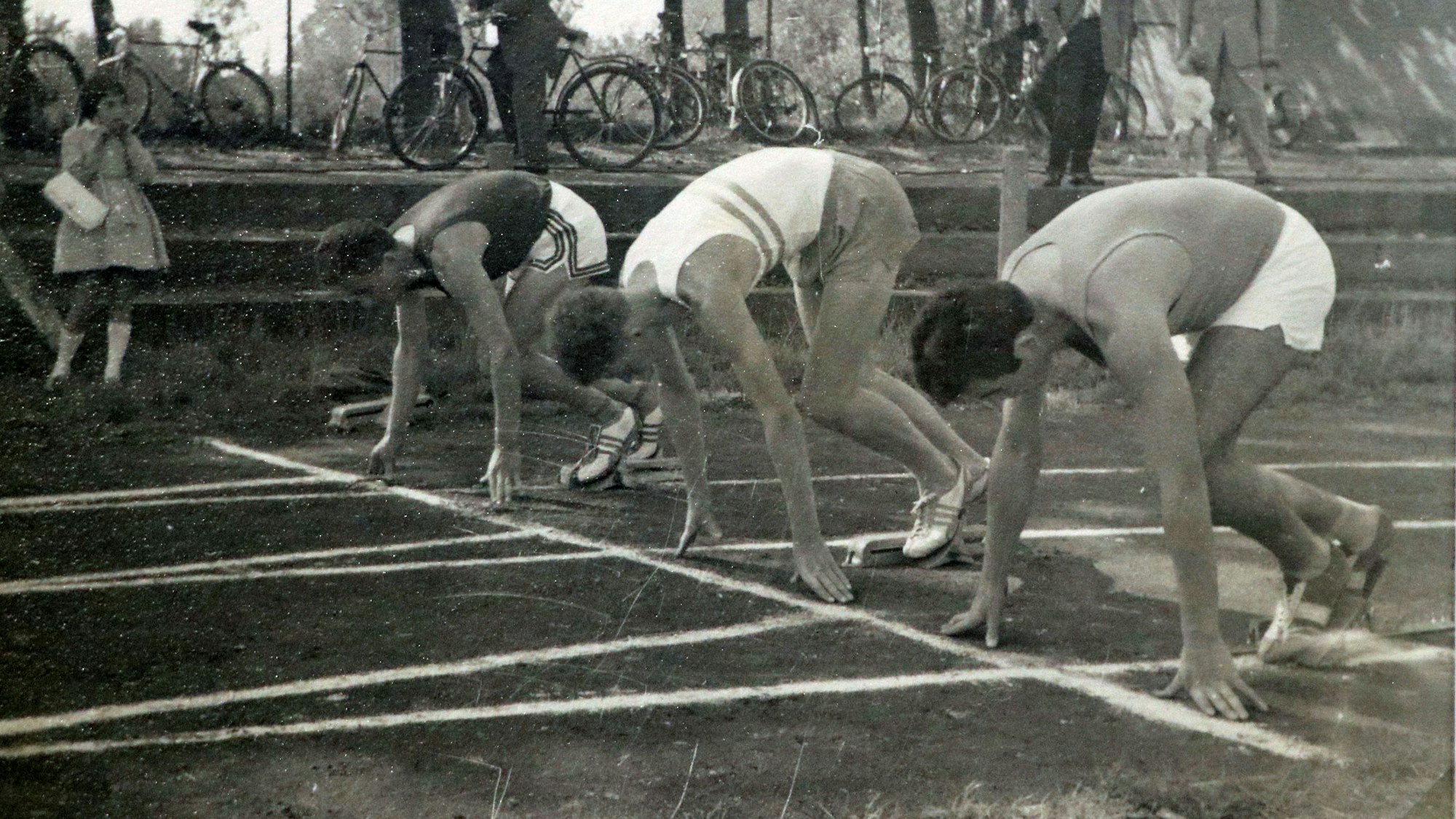 Athleten an der Startlinie auf einer Laufbahn. Das Bild ist in schwarz-weiß.
