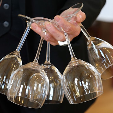 In einem Restaurant trägt eine Frau fünf Weingläser in einer Hand.