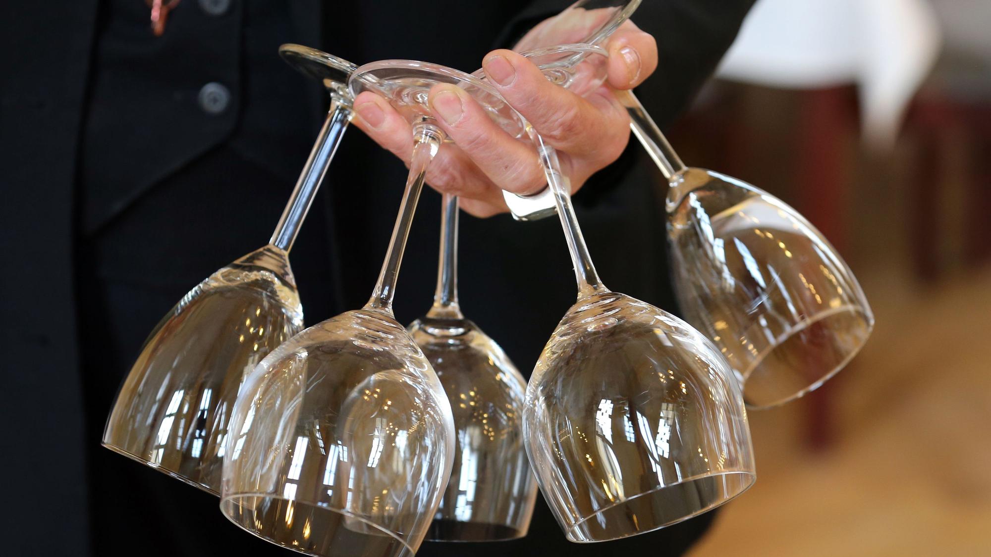 In einem Restaurant trägt eine Frau fünf Weingläser in einer Hand.