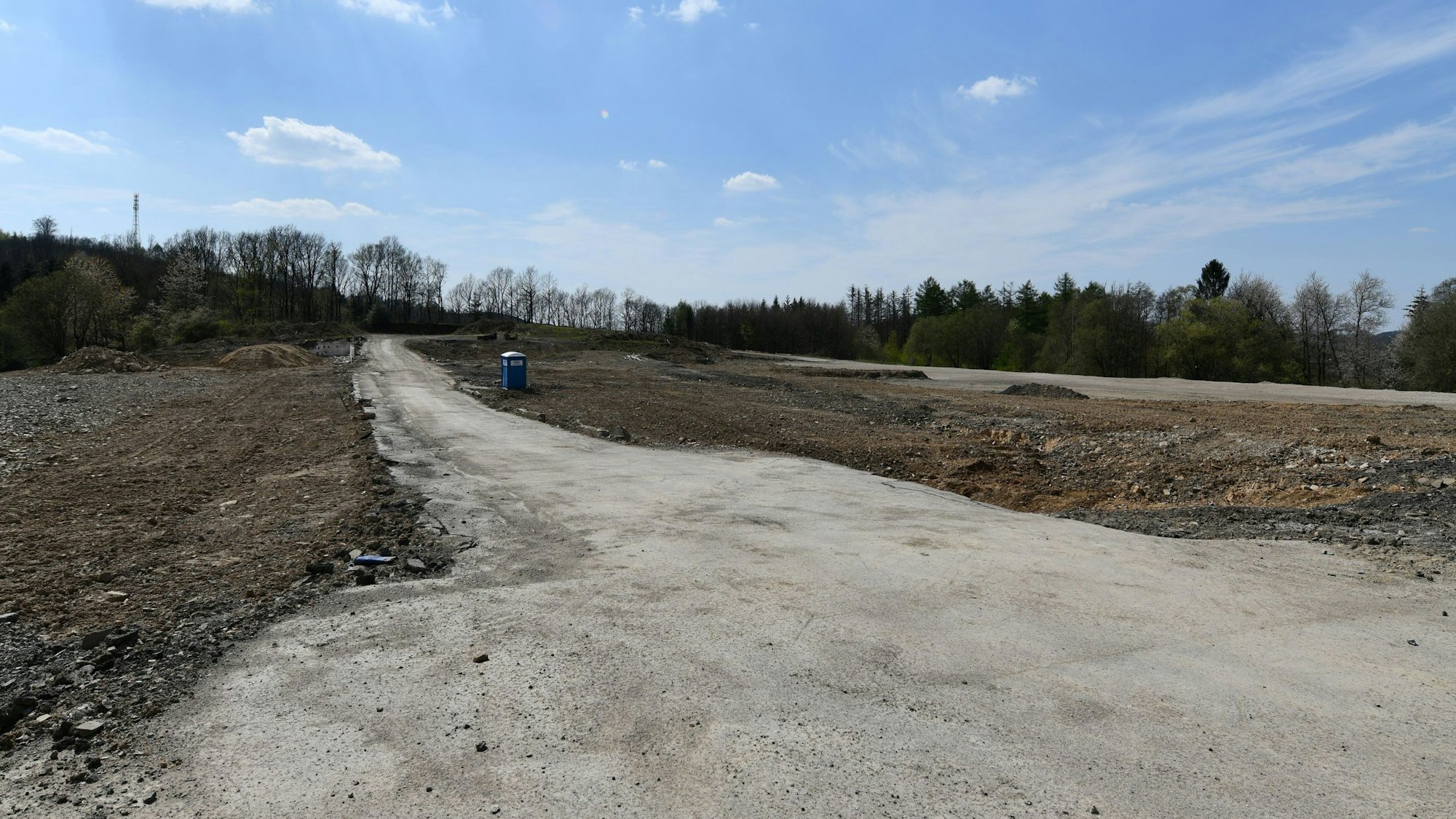 Ein braches Feld mit einem nicht-befestigten Weg und einem Dixxi-Klo