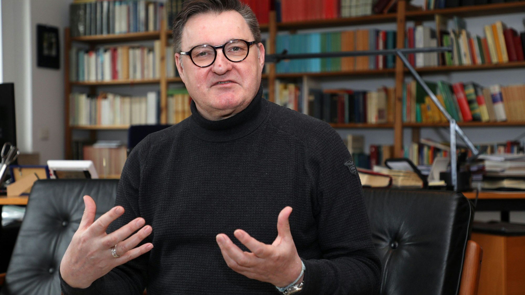 Rhein-Bergs Kreisdechant Norbert Hörter sitzt in einer Gesprächssituation in seinem Arbeitszimmer vor einer Bücherwand.
