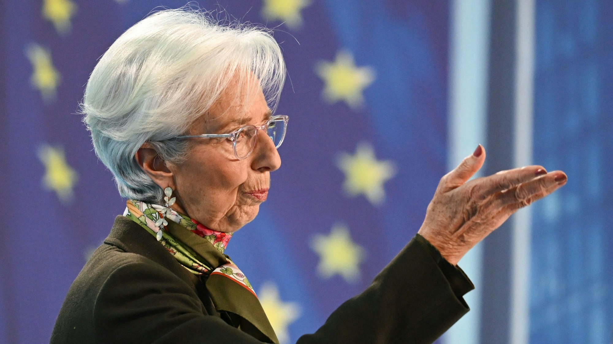 Christine Lagarde, Präsidentin der Europäischen Zentralbank (EZB), spricht während der Pressekonferenz in der EZB-Zentrale. Sie gestikuliert mit ihrer Hand. Hinter ihr sind die EU-Sterne.