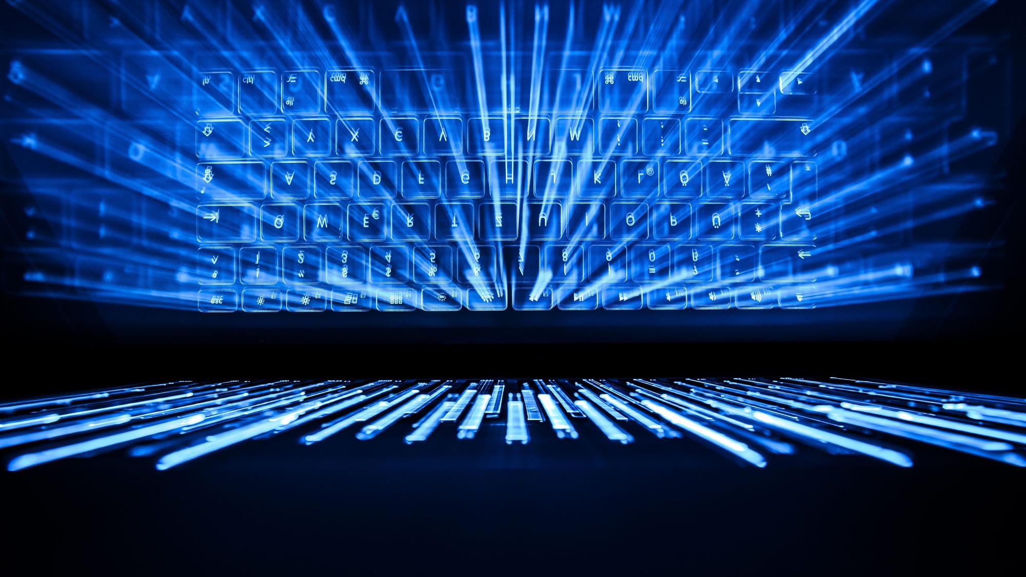 Die beleuchtete Tastatur eines Laptops spiegelt sich in einem Bildschirm.