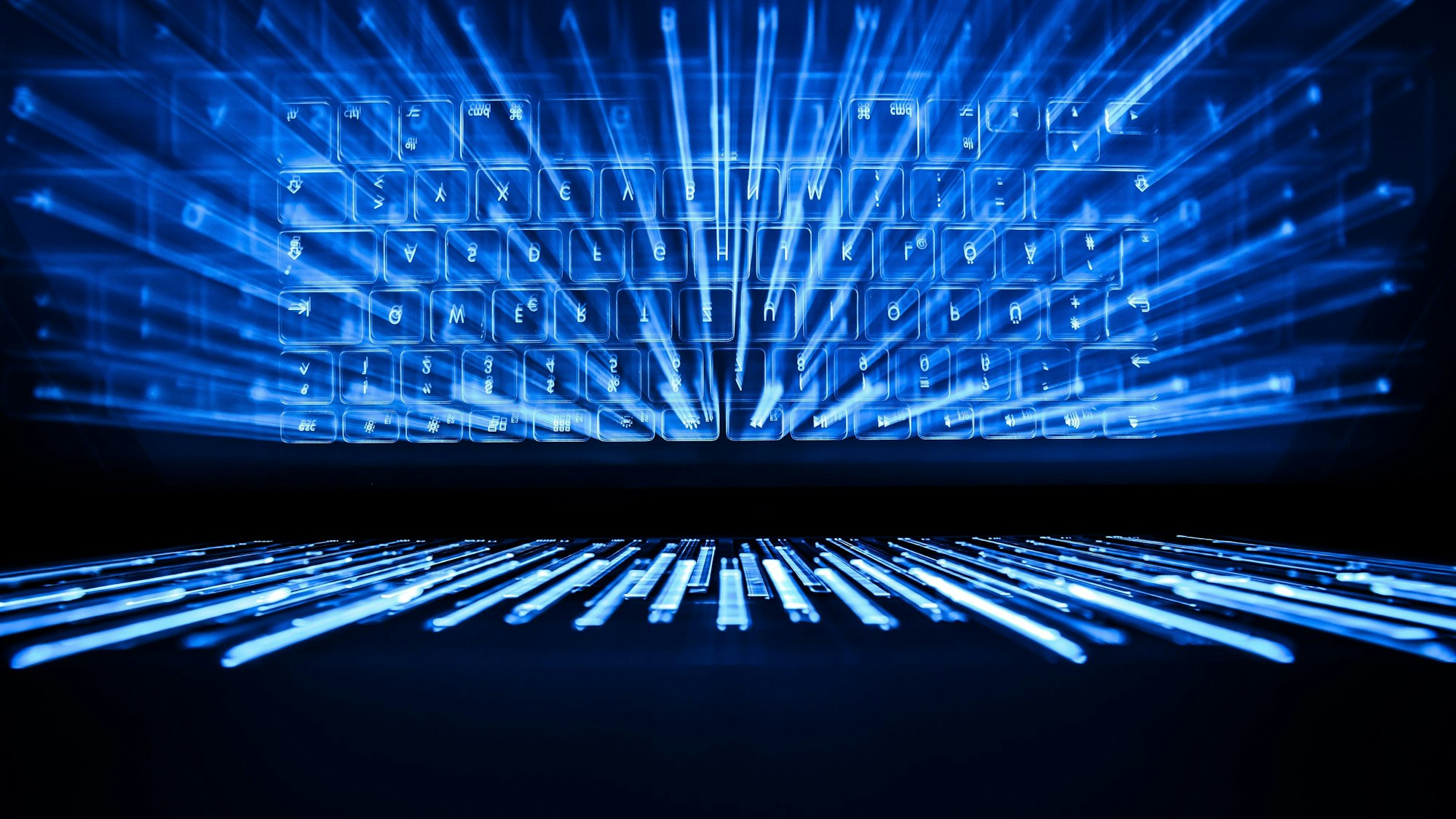 Die beleuchtete Tastatur eines Laptops spiegelt sich in einem Bildschirm.