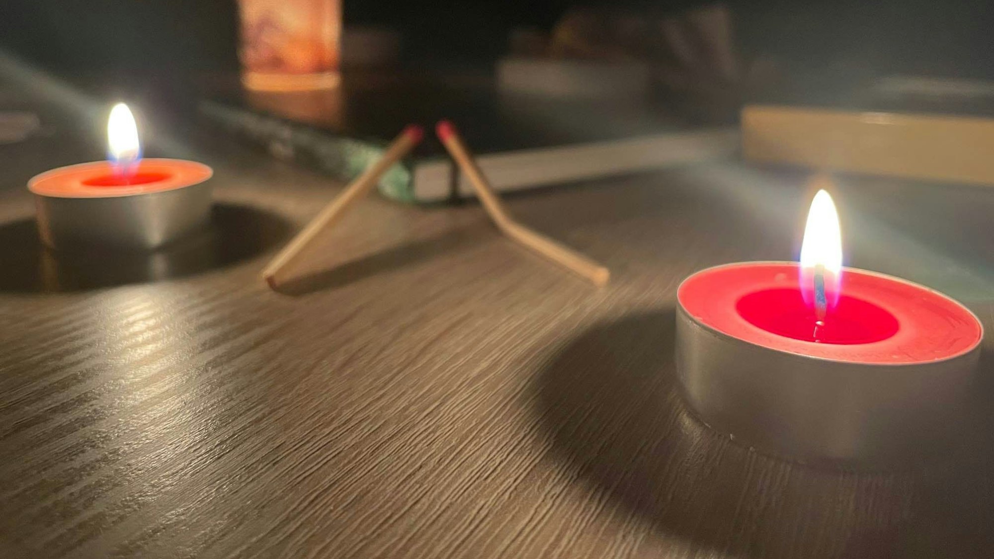 Teelichter und verbrauchte Streichhölzer stehen auf einem Tisch, die Umgebung ist dunkel.