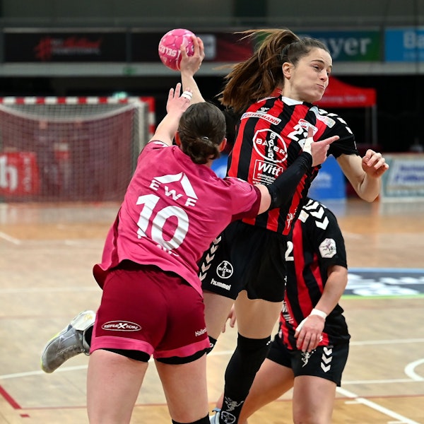 Eine Handballerin wird von ihrer Gegenspielerin beim Wurf bedrängt.