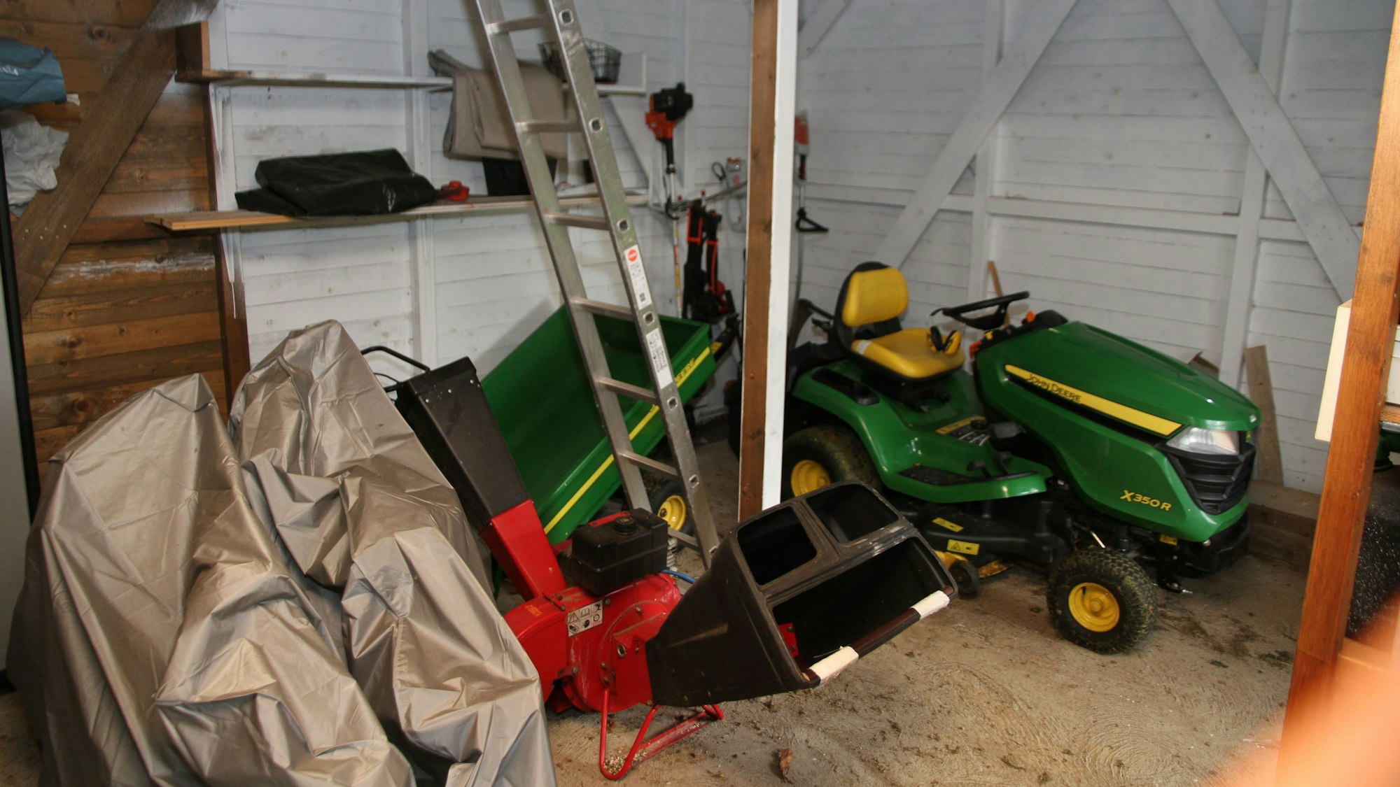 Geräte und ein Aufsichrasenmäher stehen in dem Gartenhäuschen.