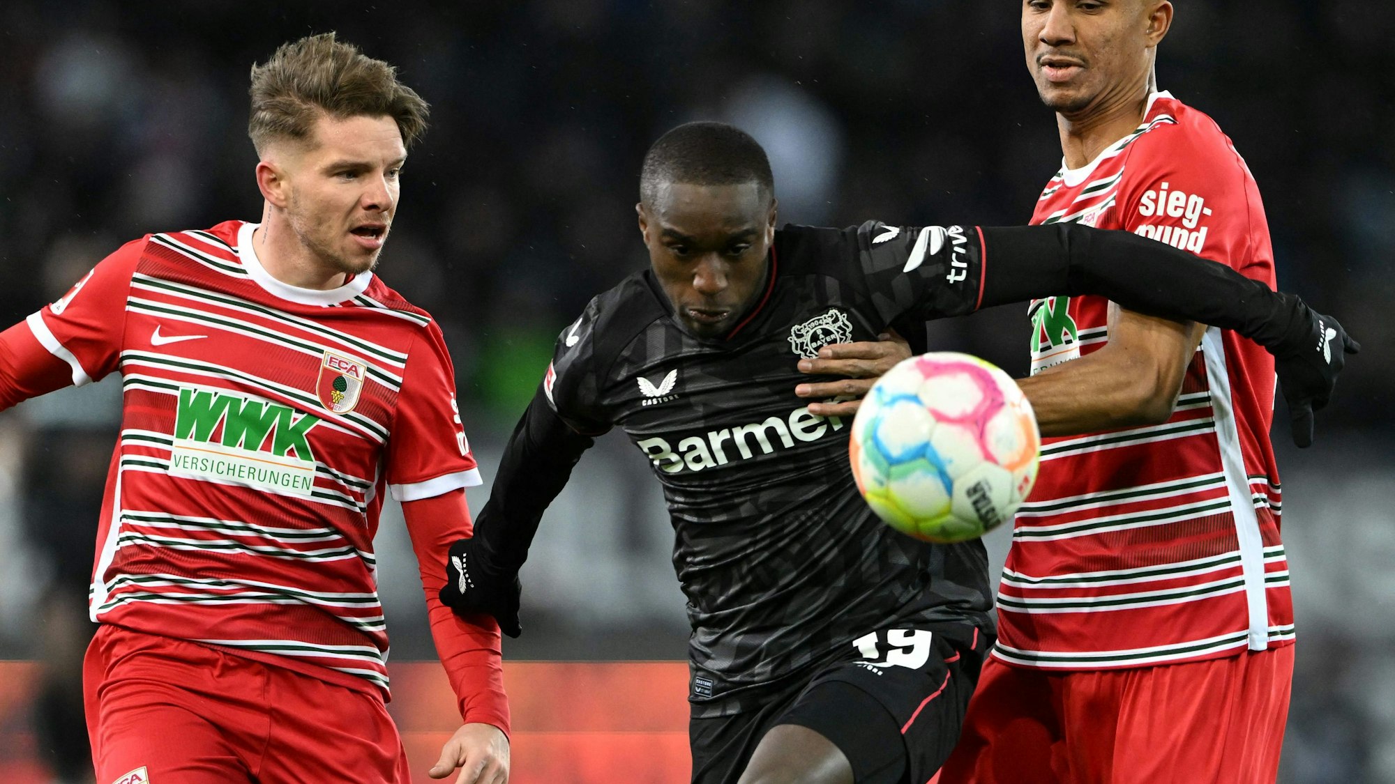 Moussa Diaby von Bayer 04 Leverkusen im Zweikampf mit zwei Spielern vom FC Augsburg.