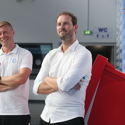 Zwei Männer in weißem Outfit stehen mit verschränkten Armen nebeneinander.