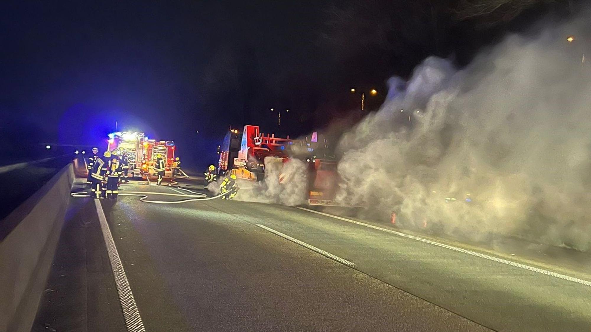 Feuerwehreinsatz auf der A61 nahe Bedburg. Feuerwehrleute und -fahrzeuge, sowie Qualm zu sehen.