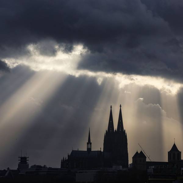 Sonnenstrahlen scheinen hinter dem Dom aus dunklen Wolken.
