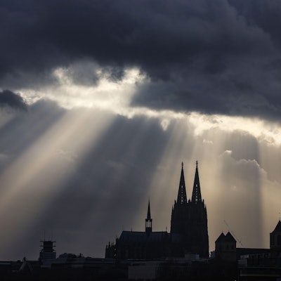 Sonnenstrahlen scheinen hinter dem Dom aus dunklen Wolken.