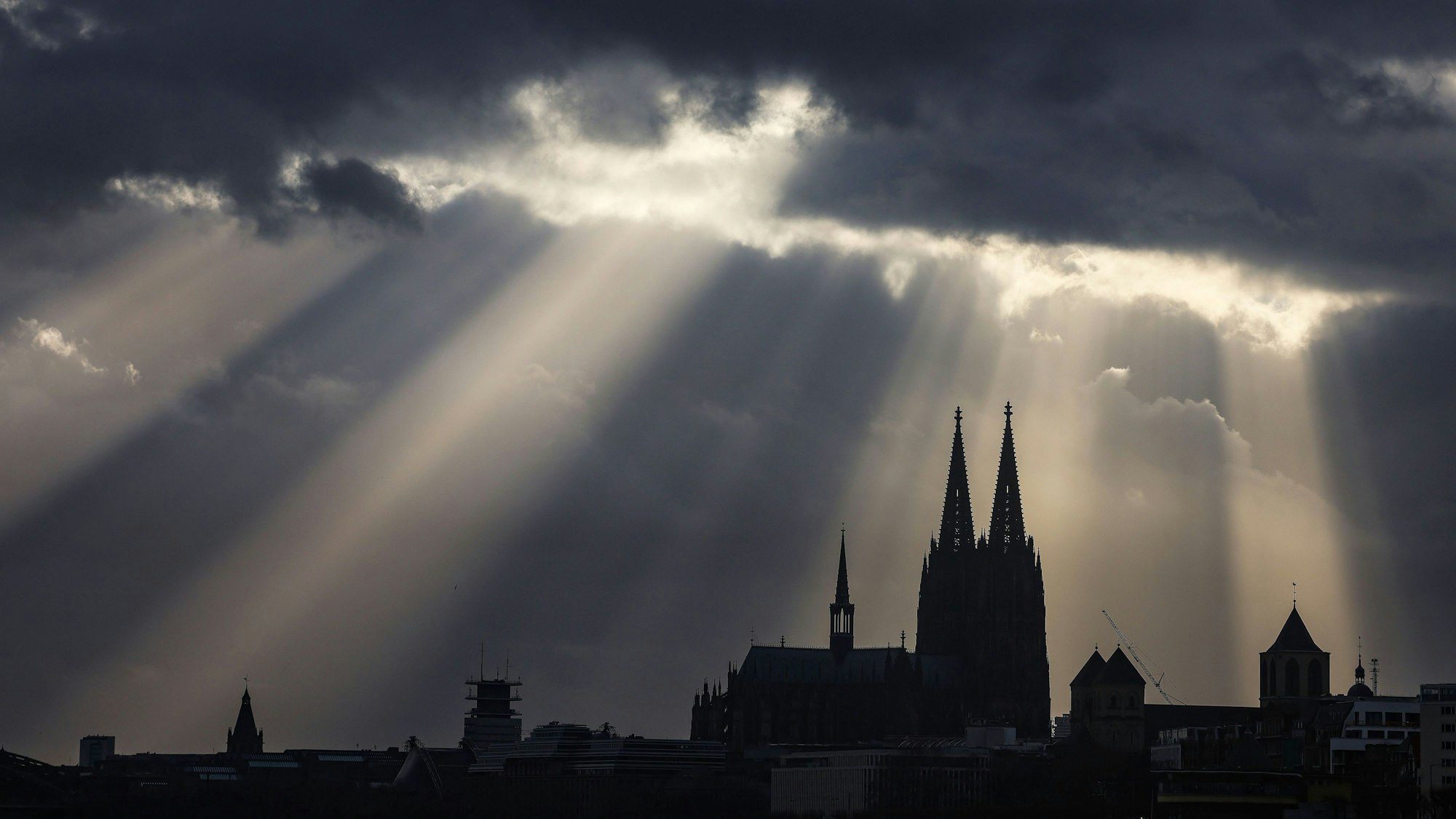 Sonnenstrahlen scheinen hinter dem Kölner Dom aus den Wolken.