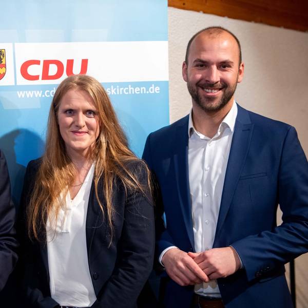 Zwei Männer und eine Frau stehen vor einem CDU-Plakat.