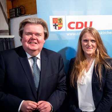 Zwei Männer und eine Frau stehen vor einem CDU-Plakat.