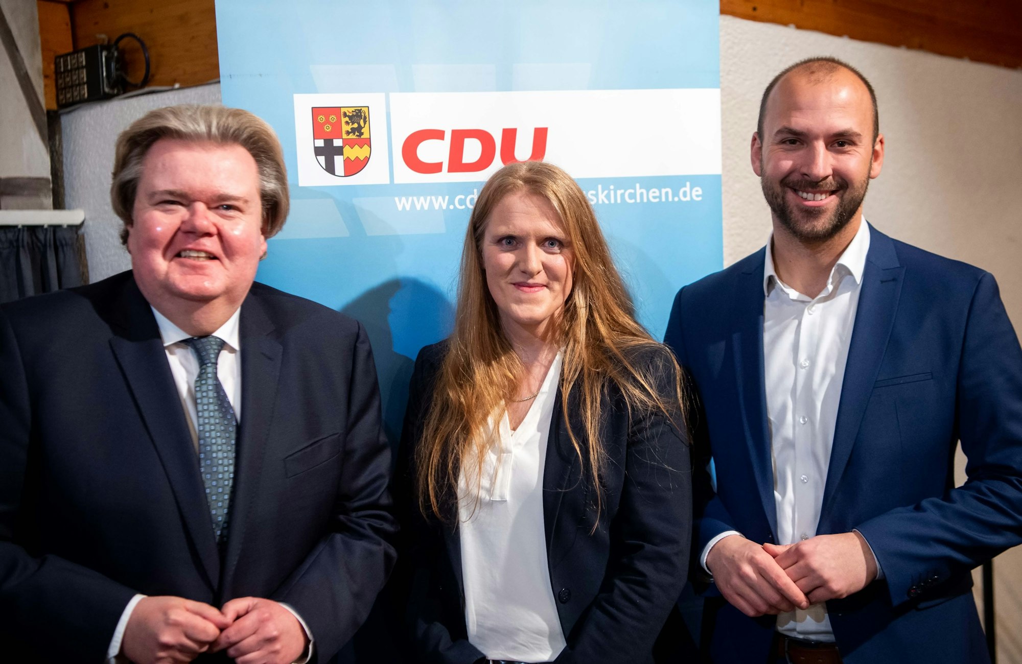 Zwei Männer und eine Frau stehen vor einem CDU-Plakat.