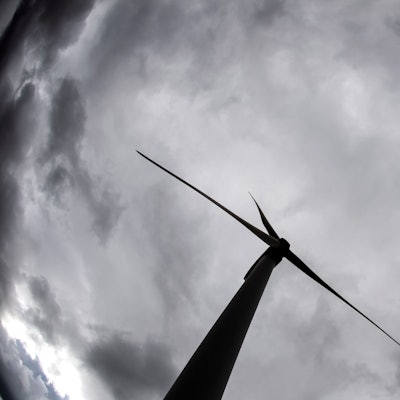 Ein Windrad ragt in den mit Wolken verhangenen Himmel.