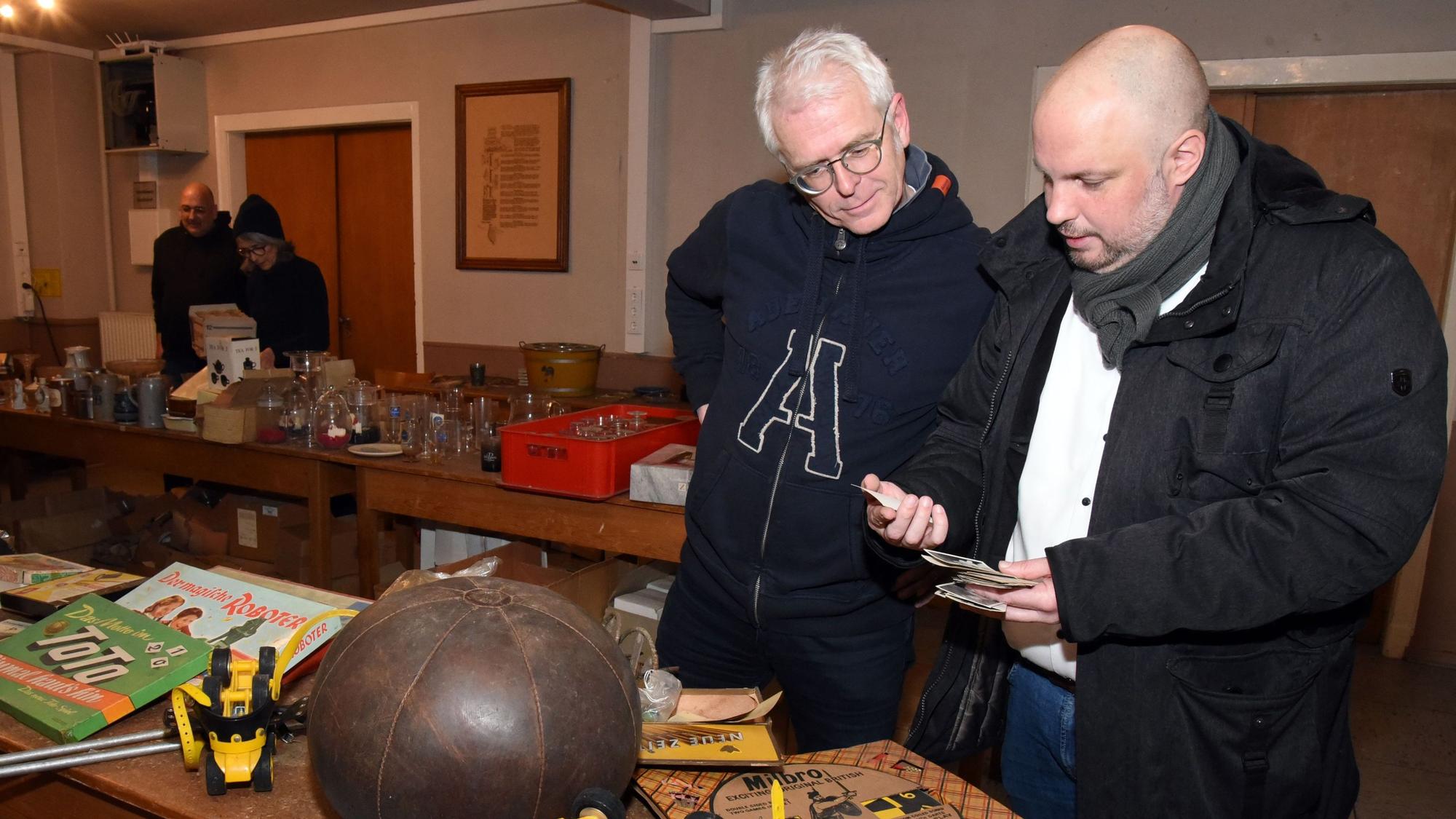 Zwei Männer betrachten auf einem Flohmarkt alte Panini-Fußballbilder aus den 1950er Jahren.