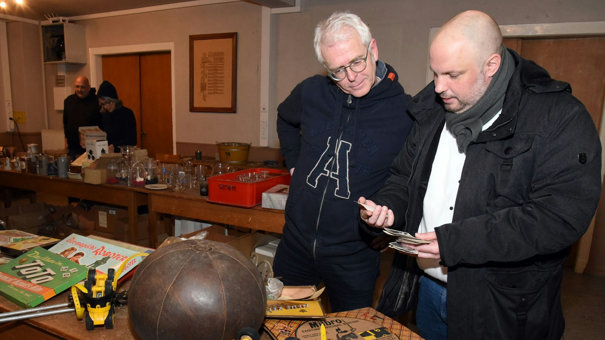 Zwei Männer betrachten auf einem Flohmarkt alte Panini-Fußballbilder aus den 1950er Jahren.