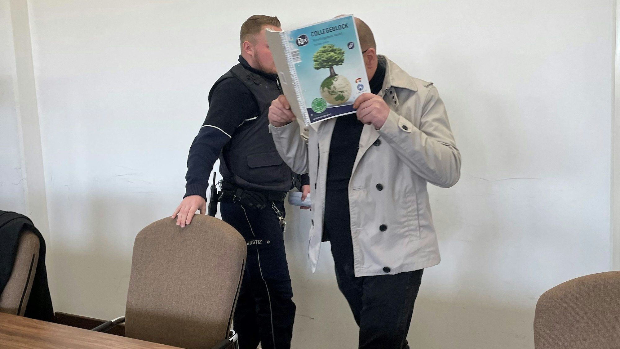 Der Angeklagte wird von einem Wachtmeister in Saal 112 des Kölner Landgerichts gebracht.