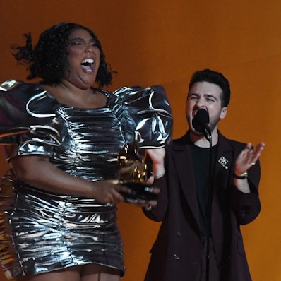 Lizzo hüpft im kurzen silbernen Kleid auf der Bühne der Grammy Awards in Los Angeles. In ihren Händen hält sie den Preis für die beste Aufnahme des Jahres.