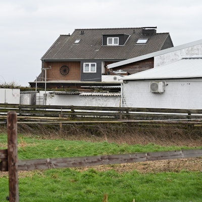 Hinter einer eingezäunten Wiese liegt ein Gebäudekomplex in weiß.