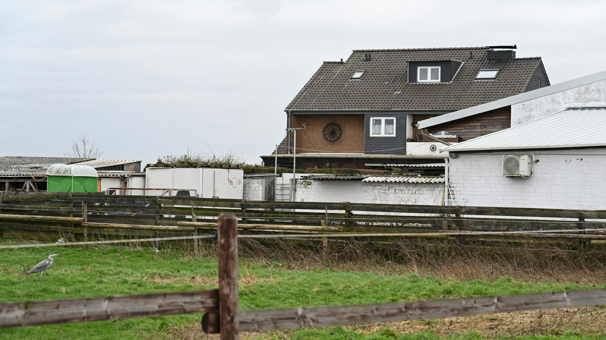 Hinter einer eingezäunten Wiese liegt ein Gebäudekomplex in weiß.