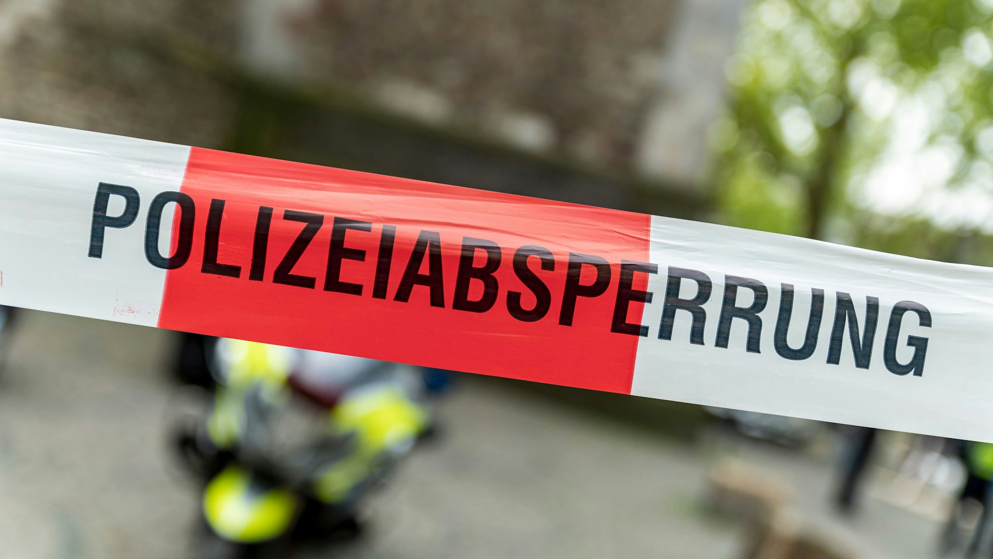 Ein rot-weißes Flatterband mit der Aufschrift „Polizeiabsperrung“ ist vor einem Motorrad der Kölner Polizei zu sehen. (Symbolbild)
