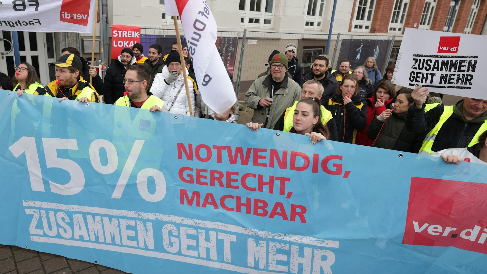 Vor einem Streiklokal demonstrieren Streikende der Post und DHL, dabei halten sie ein Banner mit der Aufschrift „15 % notwendig, gerecht, machbar, zusammen geht mehr.“