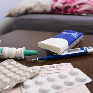 Ein Fieberthermometer, Medikamente und eine ärztliche Arbeitsunfähigkeitsbescheinigung (Krankmeldung) liegen auf einem Nachttisch