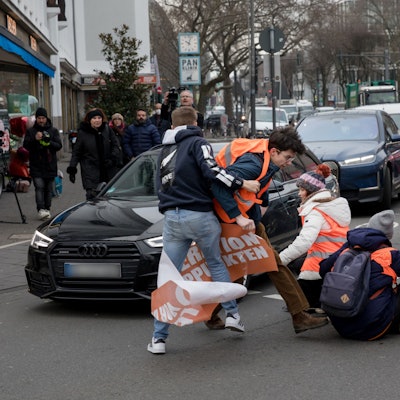 Ein Beifahrer schubst einen der Aktivisten von der Straße.