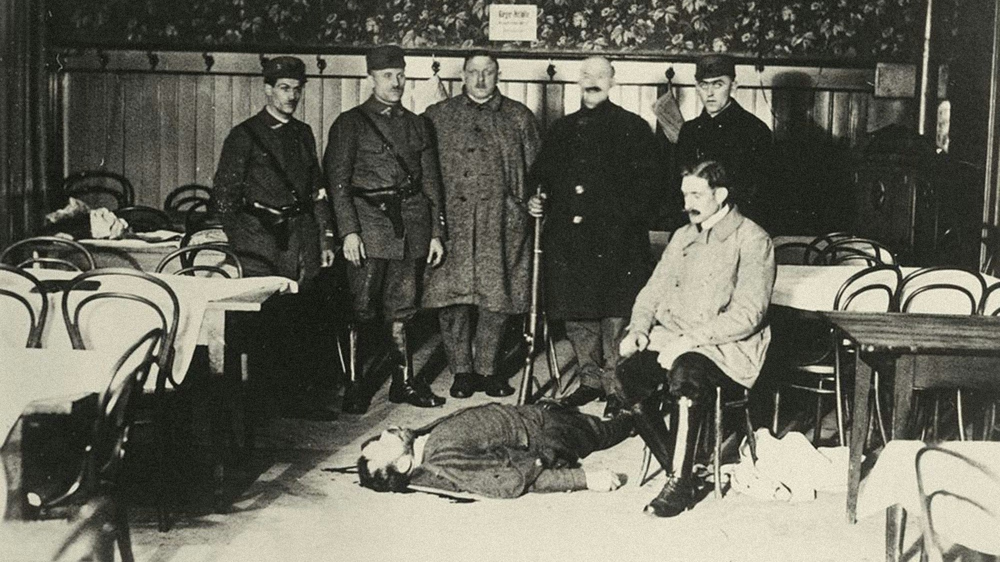 Um den am Boden liegenden Leichnam des im „Wittelsbacher Hof“ erschossenen Separatisten-Führer Heinz Orbis haben sich für ein Foto einige Anhänger gruppiert.