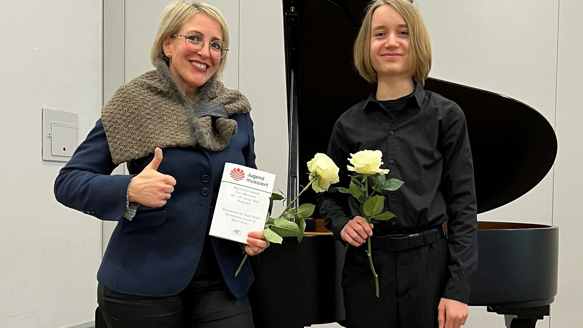 Johannes von Reuß steht mit Klavierlehrerin Judith Lenz vor einem Klavier, Urkunde und Rose in der Hand..