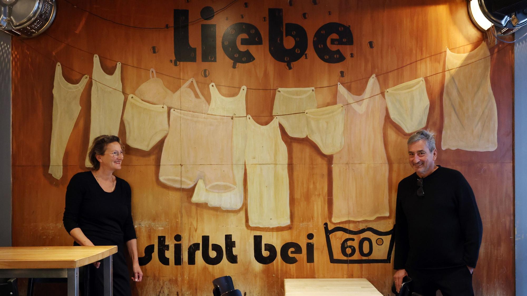 Miriam El Maani (Betriebsleiterin) und Jürgen Walter (Inhaber)
stehen vor einer Wand im Café Waschsalon.