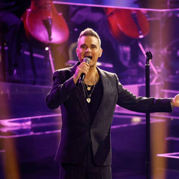 Robbie Williams steht in einem schwarzen Anzug auf der Bühne.